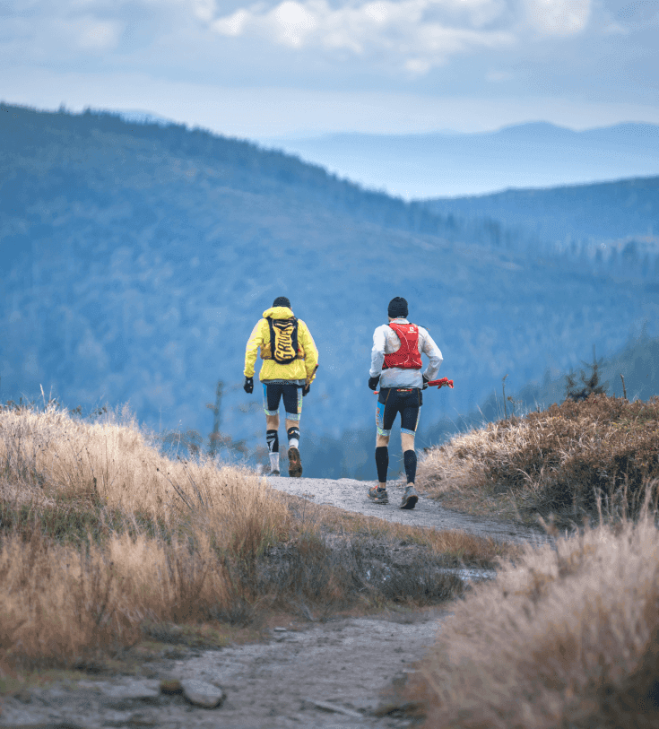 Two trail runners with backpacks on a mountain ridge path